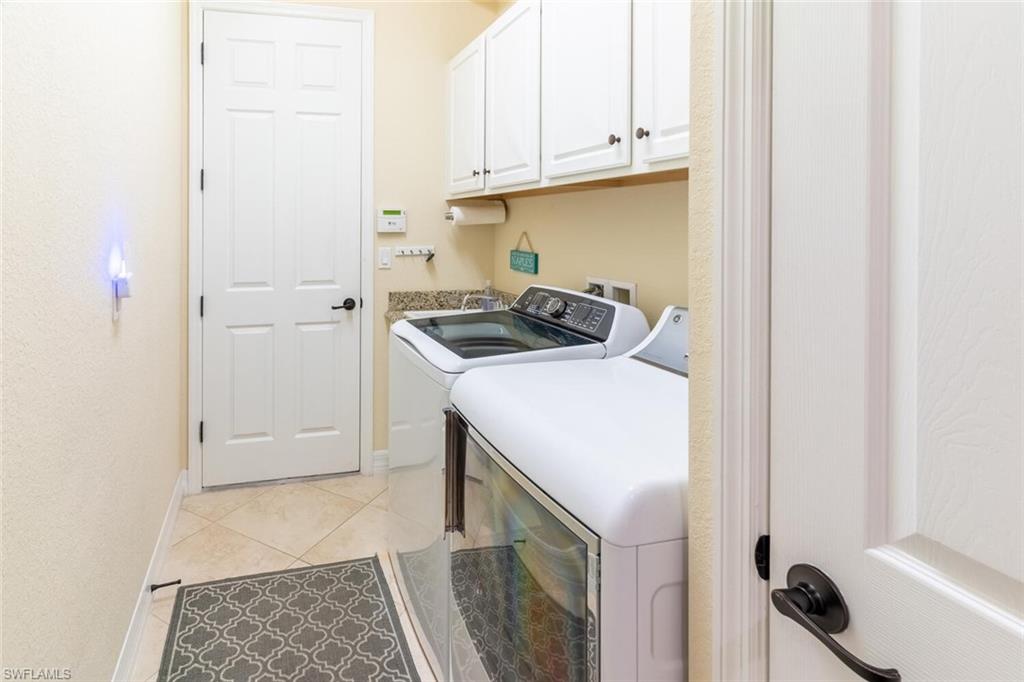 Clothes washing area with cabinets, light tile patterned floors, and washer and dryer