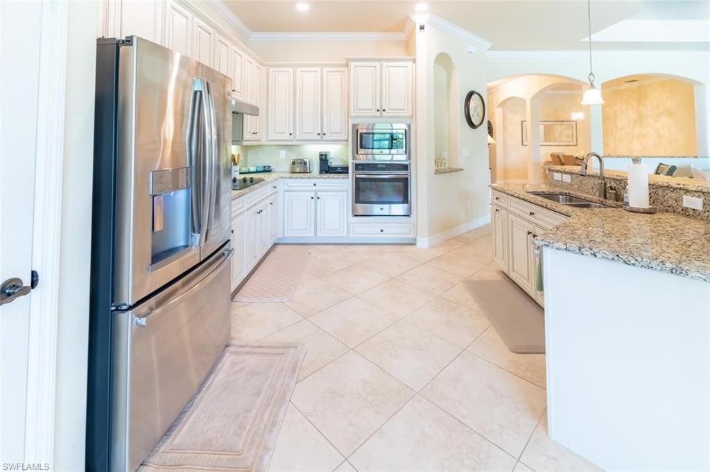 Kitchen with appliances with stainless steel finishes, light stone countertops, light tile patterned floors, ornamental molding, and sink