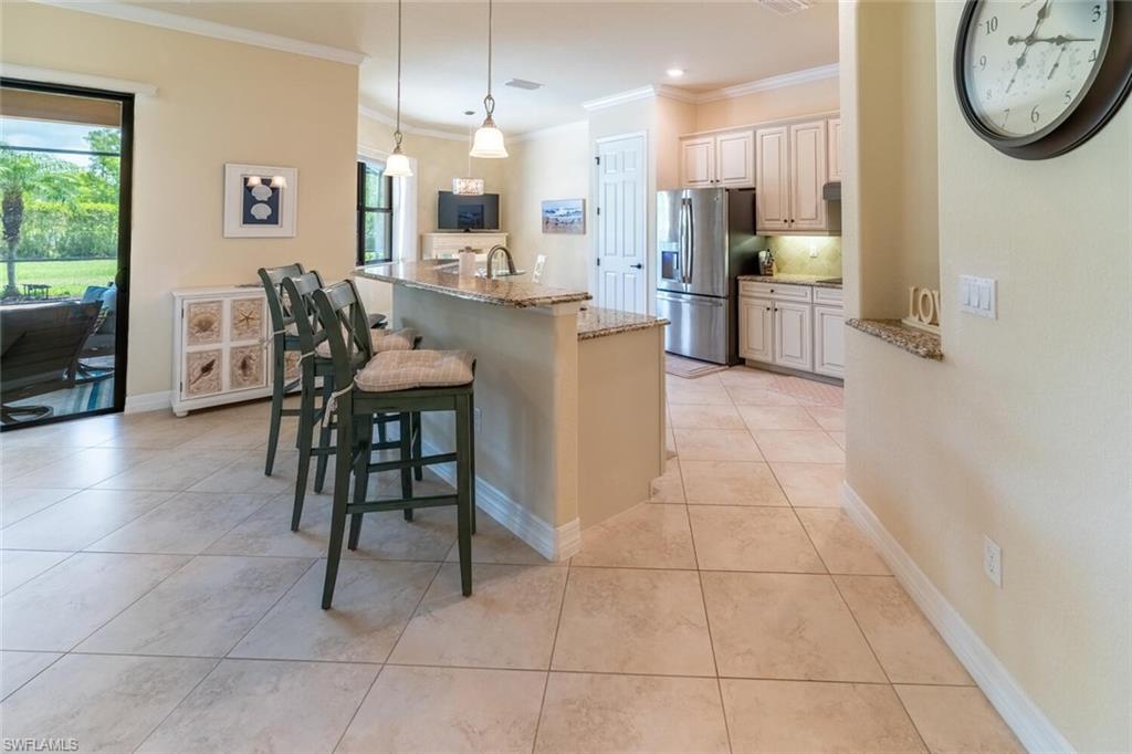 Kitchen with crown molding, stainless steel fridge with ice dispenser, a kitchen breakfast bar, light tile patterned flooring, and light stone counters