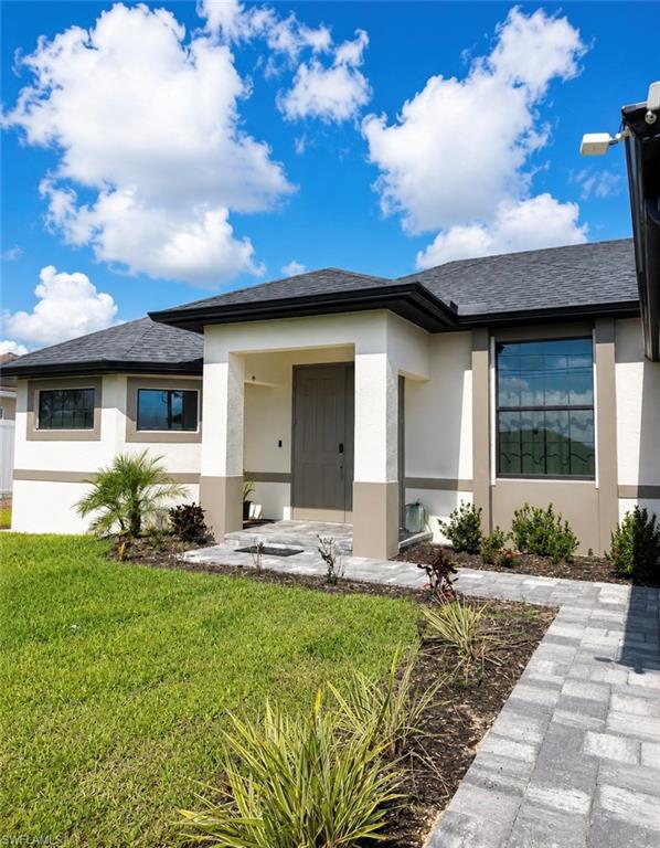 Contemporary stucco exterior featuring a covered entry, dark wood-finish front door, large picture window, and a paver walkway