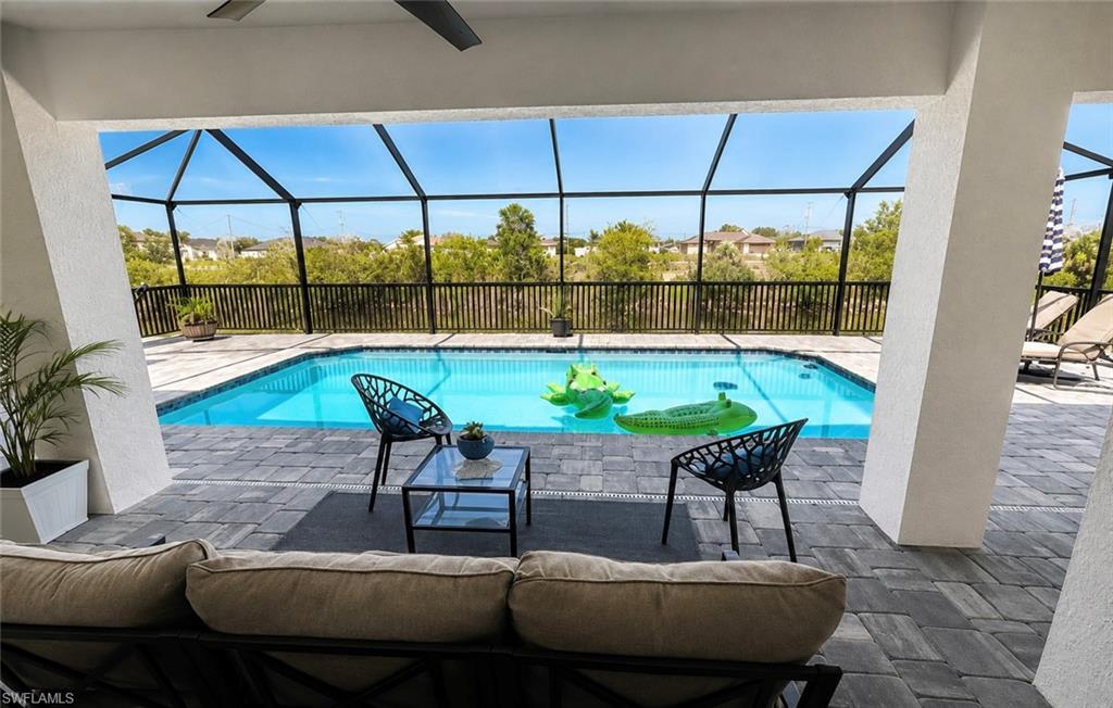 Screened outdoor living area with a paver patio and a rectangular swimming pool, featuring a ceiling fan and a black metal fence