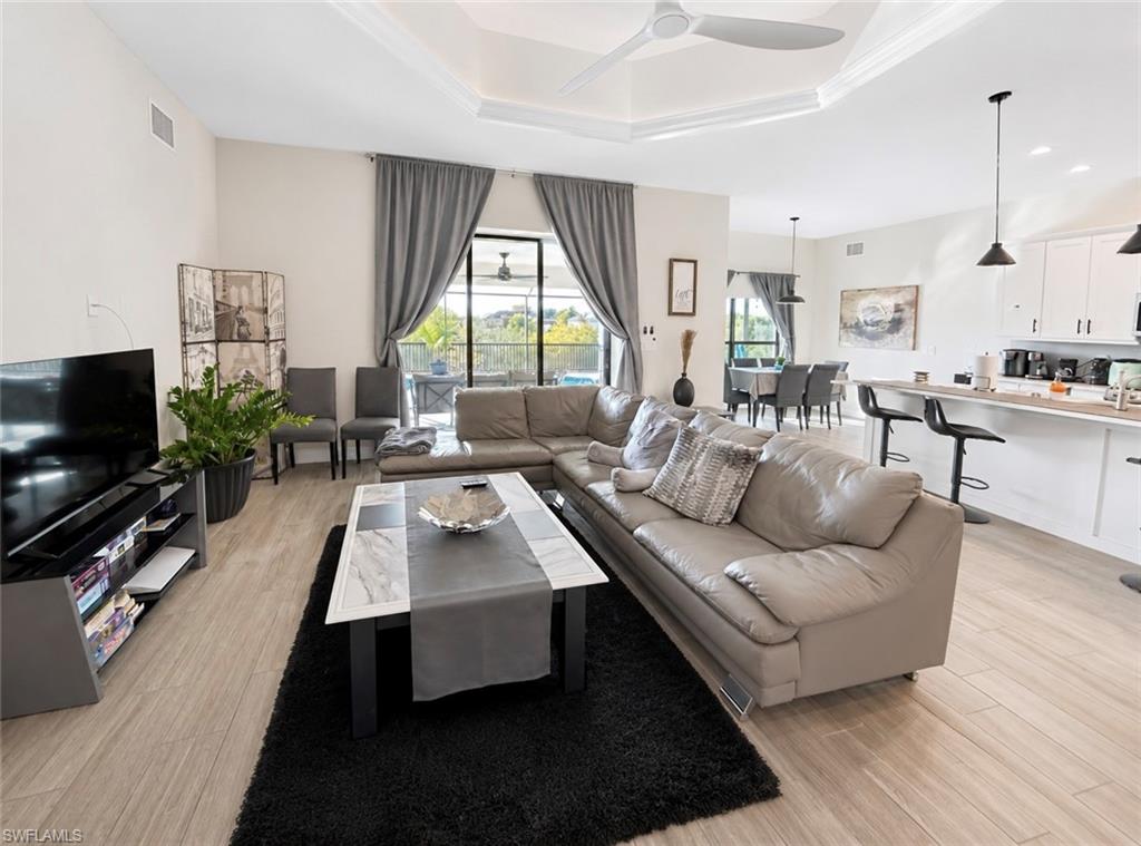 Open-concept living area featuring wood-finish flooring, a tray ceiling with a modern ceiling fan, and large sliding glass doors leading to an outdoor space