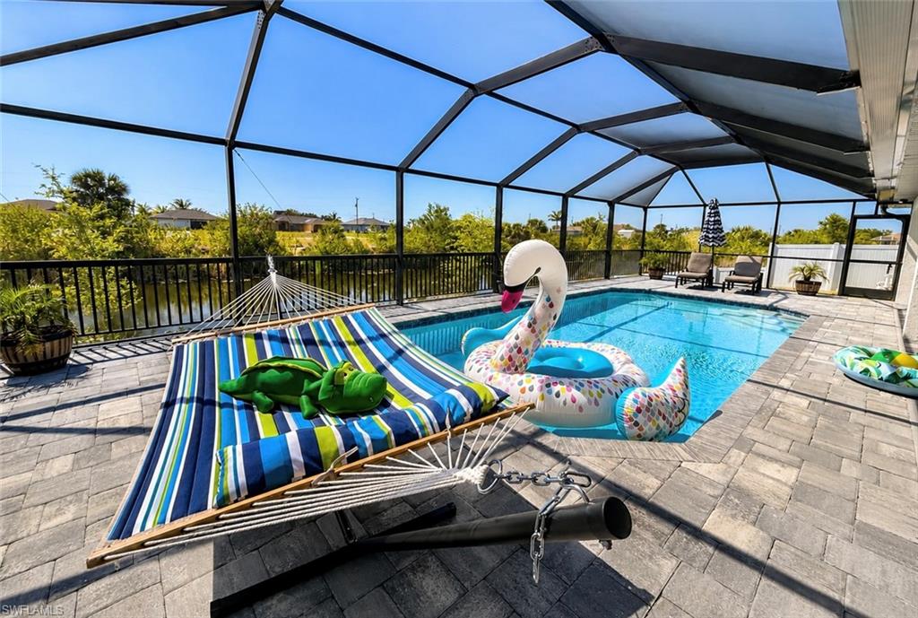 Screened-in pool deck featuring paver flooring, a sparkling swimming pool, and a black metal fence bordering a natural water feature