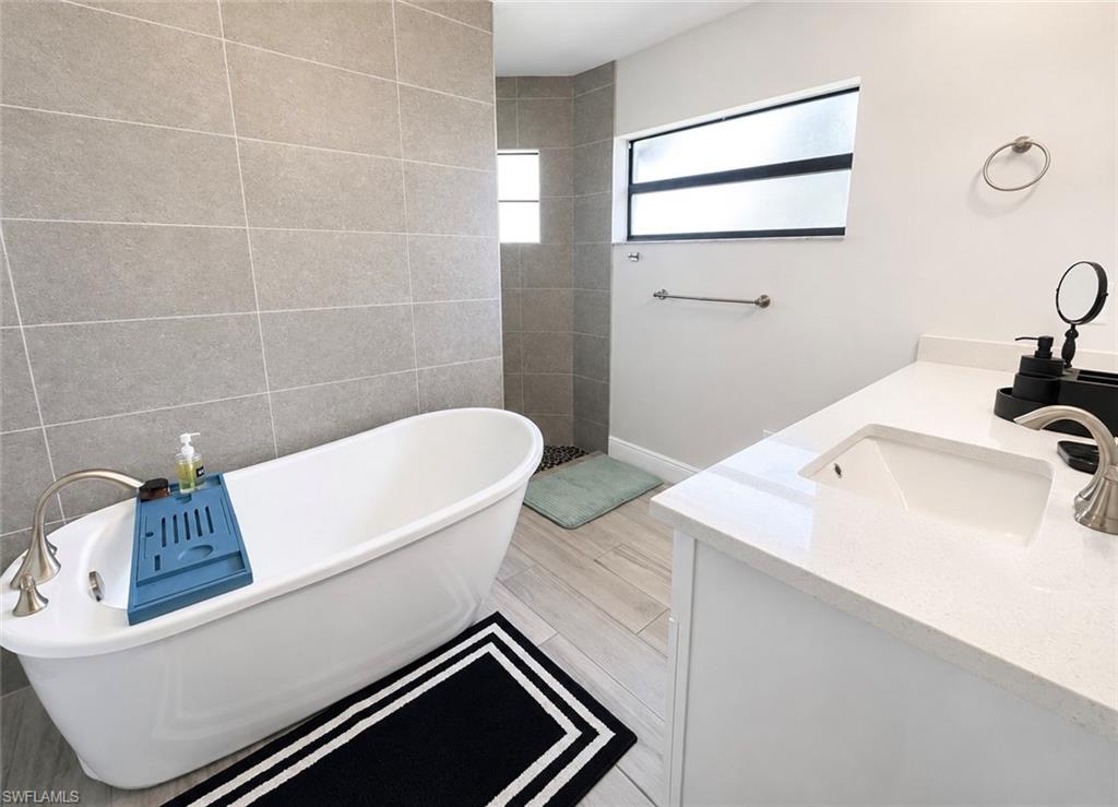 Freestanding soaking tub with a brushed nickel faucet, light wood-finish flooring, and a single vanity with an undermount sink and quartz countertop