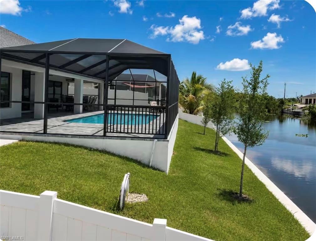 Screened-in pool enclosure with a paved deck, bordered by a manicured lawn and a canal