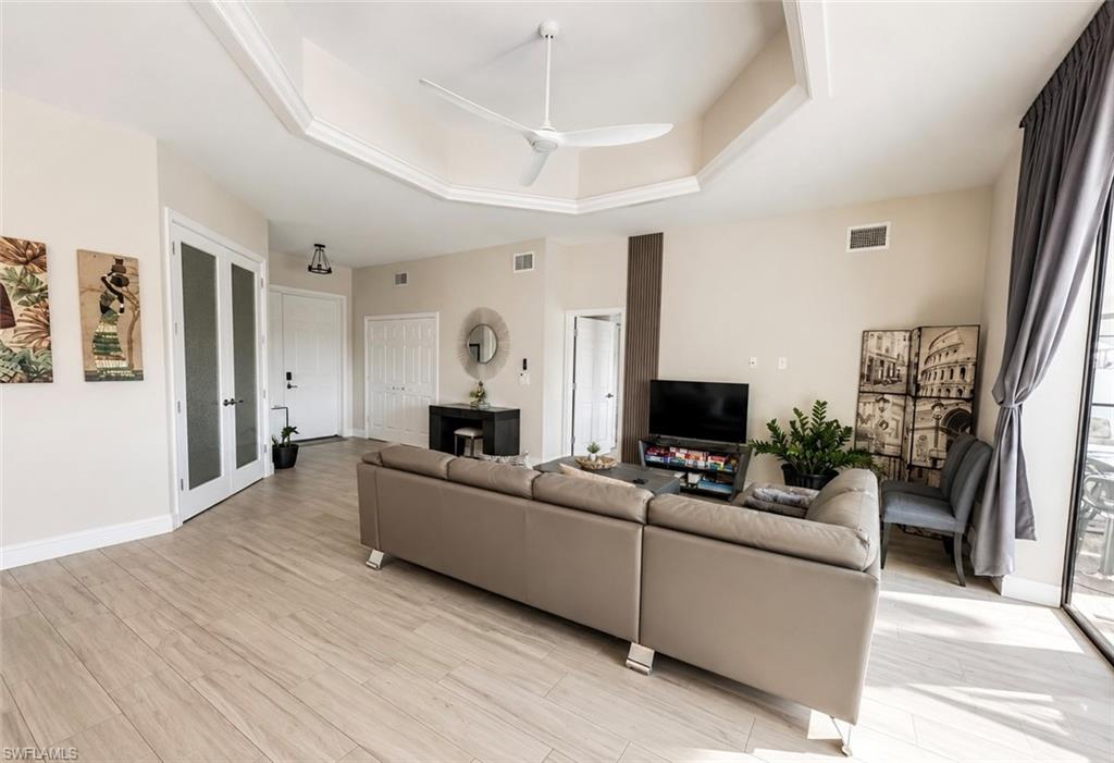 Spacious living area featuring wood-finish flooring, a tray ceiling with crown molding, and an integrated ceiling fan