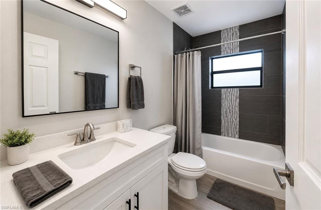 White vanity with brushed nickel fixtures, a rectangular mirror, a white bathtub, and dark subway tile with an accent strip