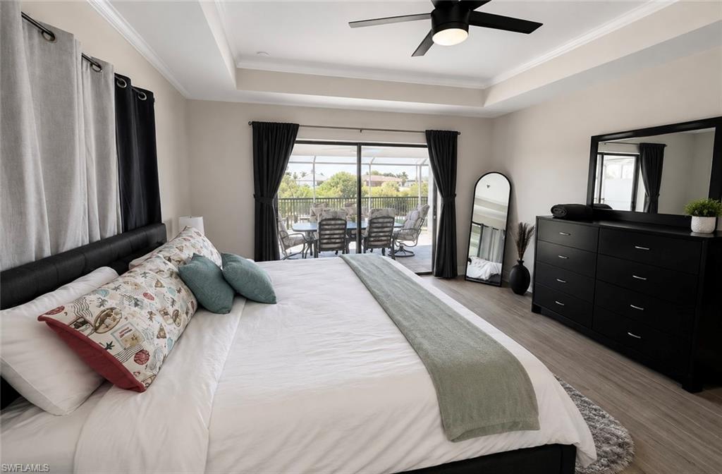 Tray ceiling with crown molding, ceiling fan with integrated lighting, wood-finish flooring, sliding glass door with exterior access, and dark curtain panels
