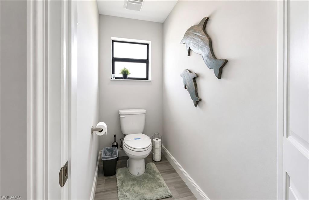 Powder room featuring a single toilet, small window, baseboard trim, and wood-finish flooring