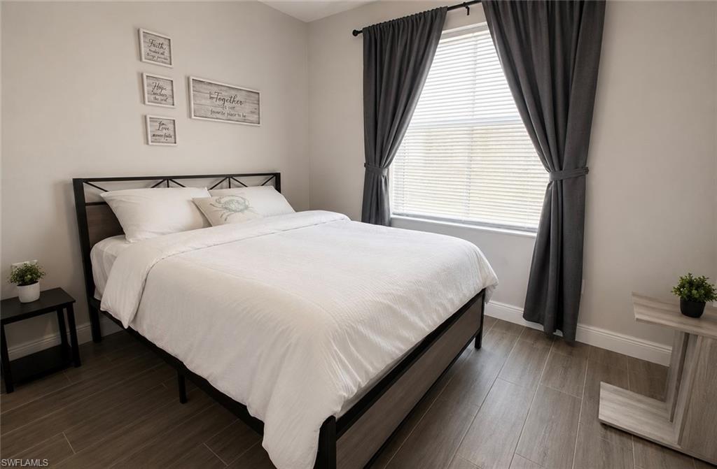 Bright bedroom featuring a black metal bed frame, wood-finish flooring, and large window with thermal-lined curtains