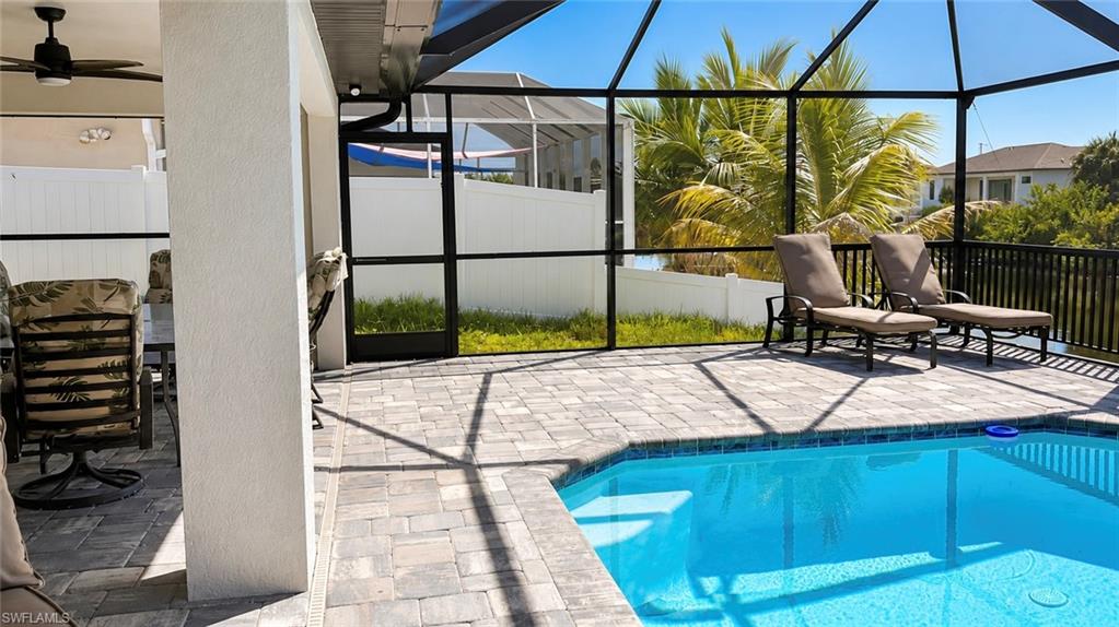 Screened outdoor living area featuring a rectangular pool with integrated steps, paver decking, and a ceiling fan