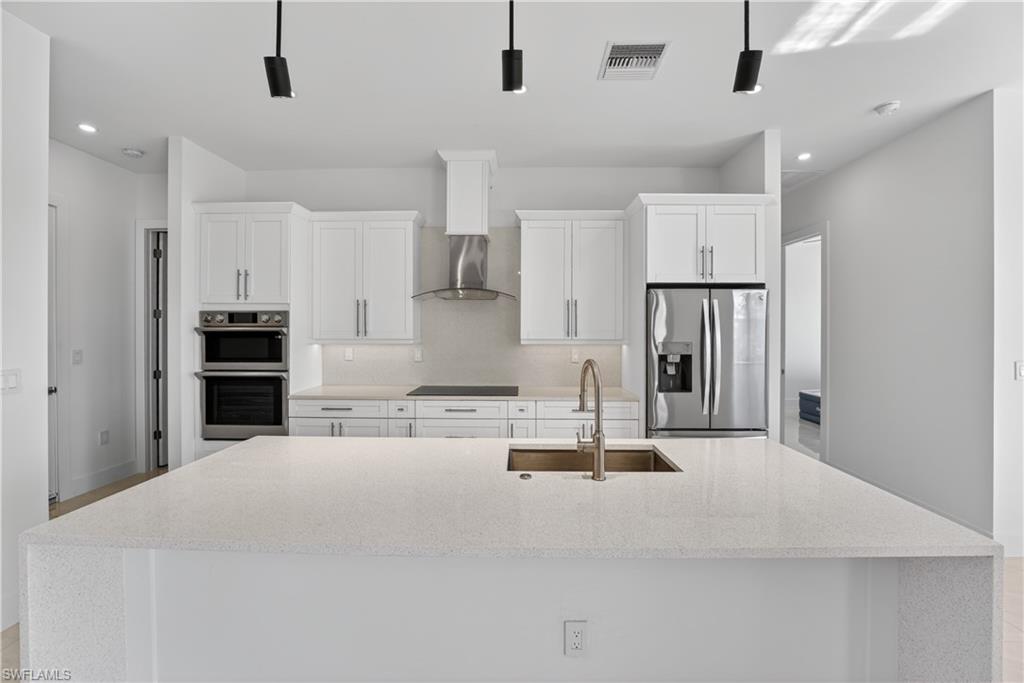 Spacious kitchen featuring an expansive island with an undermount sink, stainless steel appliances, white cabinetry, a built-in double oven, and pendant lighting
