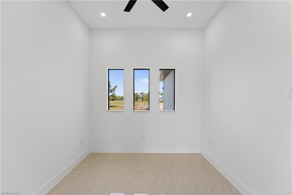 Bright interior space featuring three vertical windows, recessed lighting, a ceiling fan, light tile flooring, and white baseboards