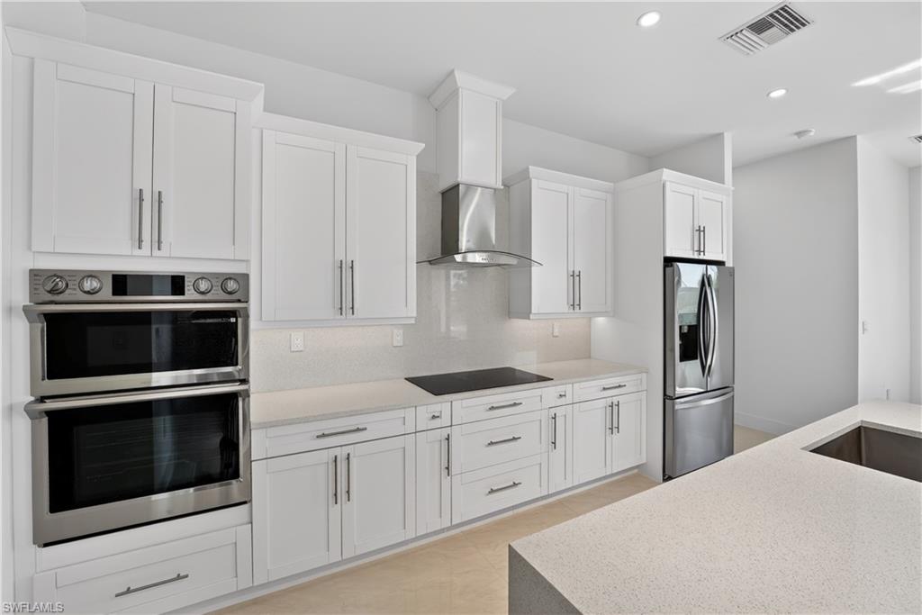 Bright kitchen featuring white shaker cabinetry, stainless steel appliances, a built-in double oven, a stainless steel range hood, and light-toned countertops