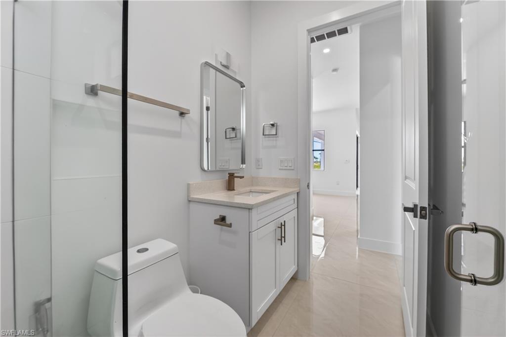 Contemporary bathroom featuring a frameless glass shower enclosure, a single vanity with stone countertop, and a sleek rectangular mirror