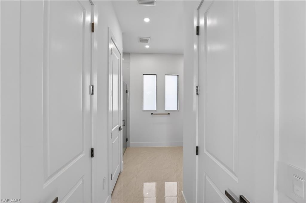 Bright hallway featuring recessed lighting, light-toned tile flooring, white paneled doors with dark hardware, and two vertical windows at the far end