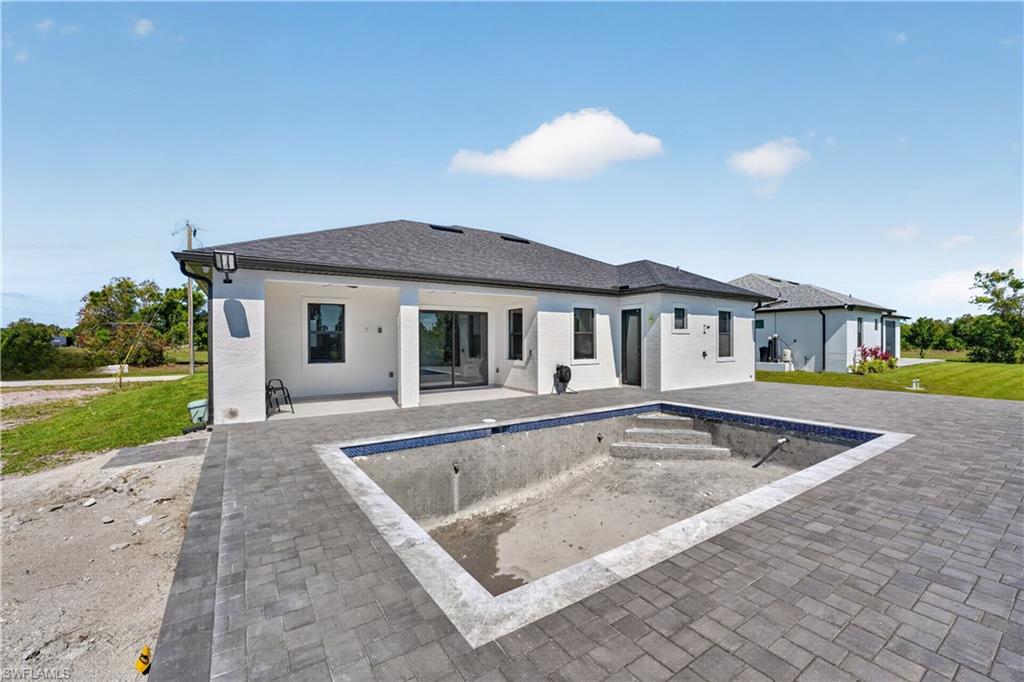 Rear exterior featuring a large paver patio, a rectangular pool shell with internal steps, and multiple sliding glass doors