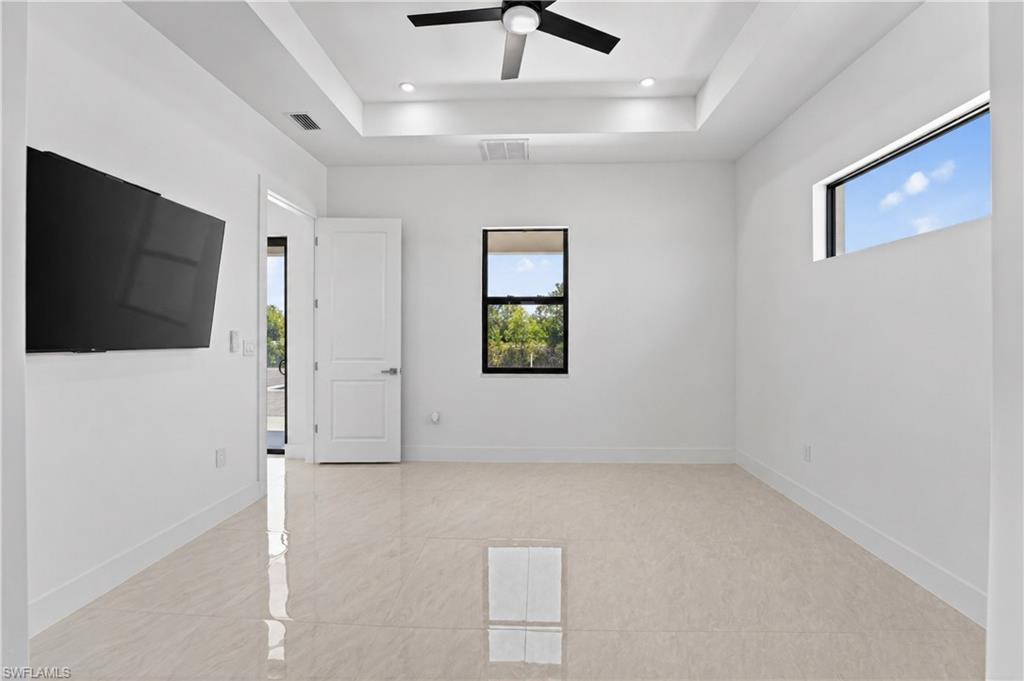 Spacious room featuring light-toned tile flooring, a tray ceiling with recessed lighting, and a ceiling fan