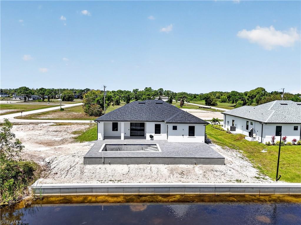 Rear exterior featuring a black shingle roof, white stucco walls, and a paver patio with an integrated pool
