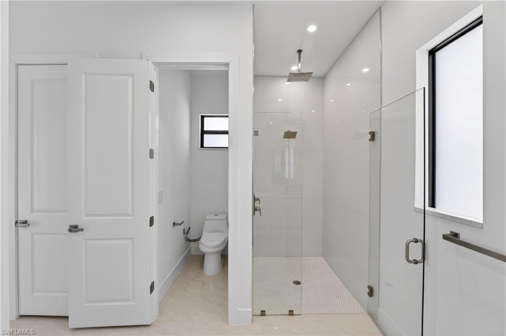 Modern bathroom featuring a glass-enclosed shower with a rainfall showerhead, white subway tile walls, and a white penny tile floor