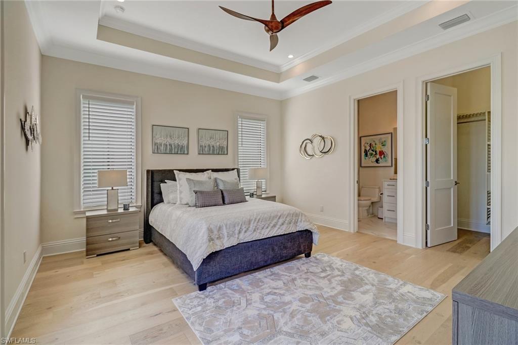 Bedroom featuring a raised ceiling, connected bathroom, ceiling fan, and light wood-type flooring