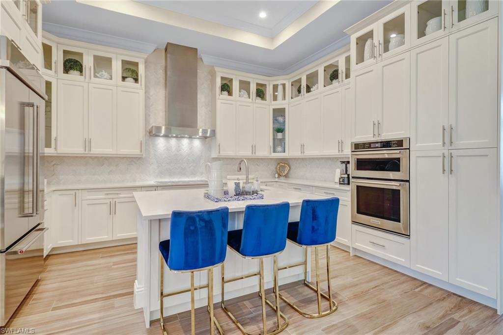 Kitchen featuring appliances with stainless steel finishes, backsplash, wall chimney exhaust hood, a raised ceiling, and a center island with sink