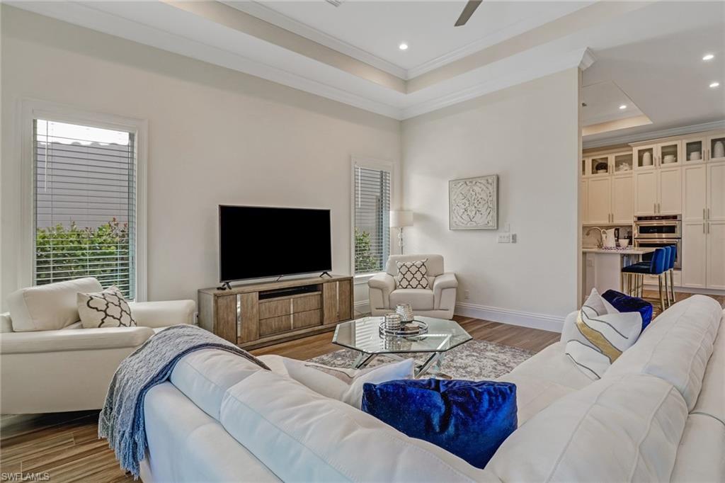 Living room with a raised ceiling, ceiling fan, light hardwood / wood-style floors, and ornamental molding