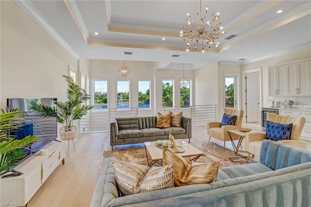Living room with a tray ceiling, beverage cooler, crown molding, a notable chandelier, and light hardwood / wood-style floors