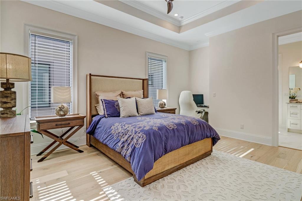 Bedroom with a raised ceiling, connected bathroom, light hardwood / wood-style flooring, and ornamental molding