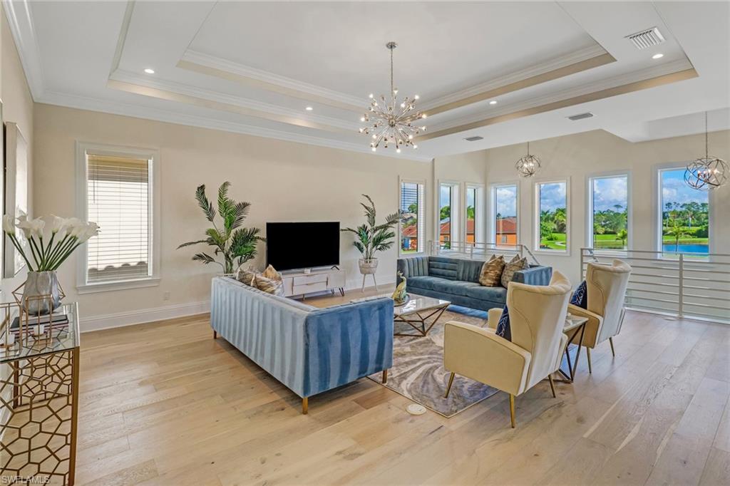 Living room with light hardwood / wood-style floors, crown molding, and a tray ceiling