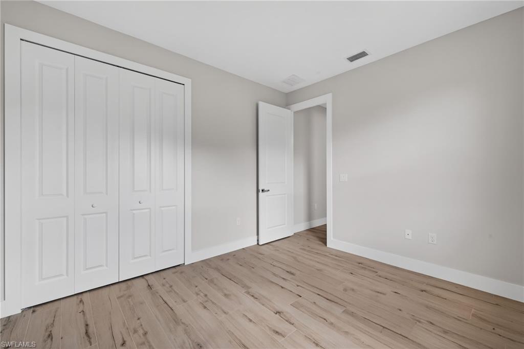 Neutral tone wall paint, wood-finish flooring, white bi-fold closet doors, white baseboards, and a white interior door with dark hardware