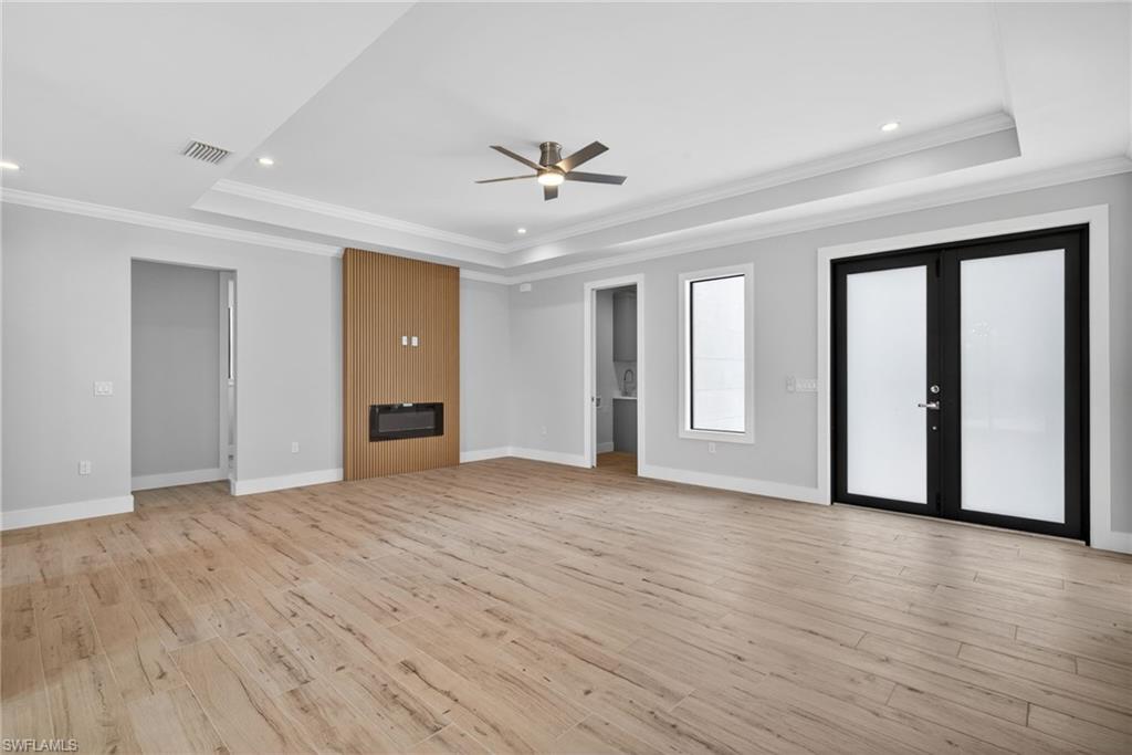 Spacious interior with wood-finish flooring, a contemporary electric fireplace with a wood panel surround, and a tray ceiling