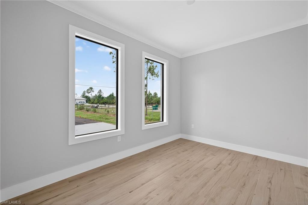 Light gray walls with white trim, wood-finish flooring, two vertical windows with white frames, and white crown molding