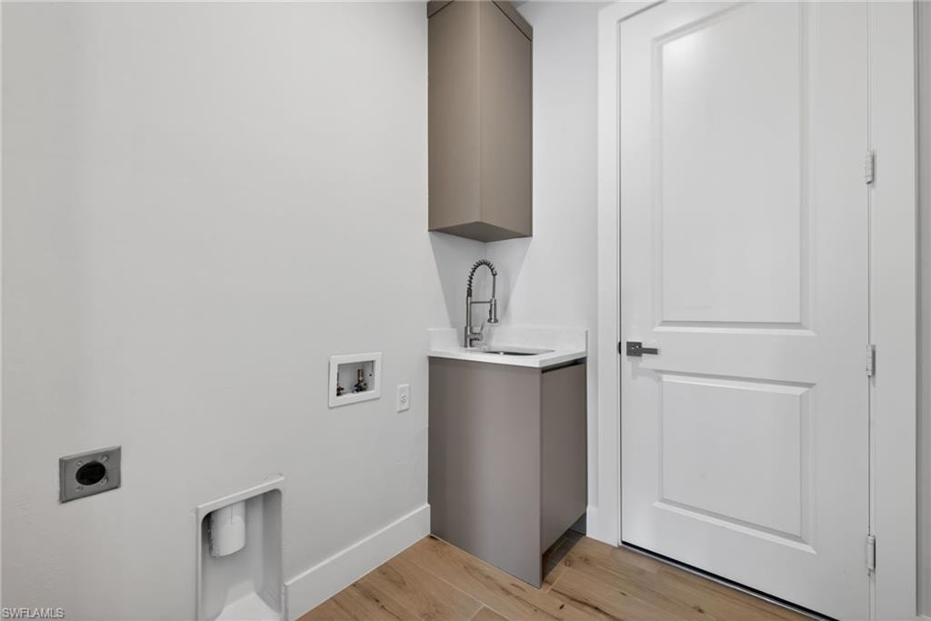 Dedicated laundry area featuring wood-finish flooring, a utility sink with a gooseneck faucet, light gray cabinetry, white countertops, and a paneled interior door with dark hardware
