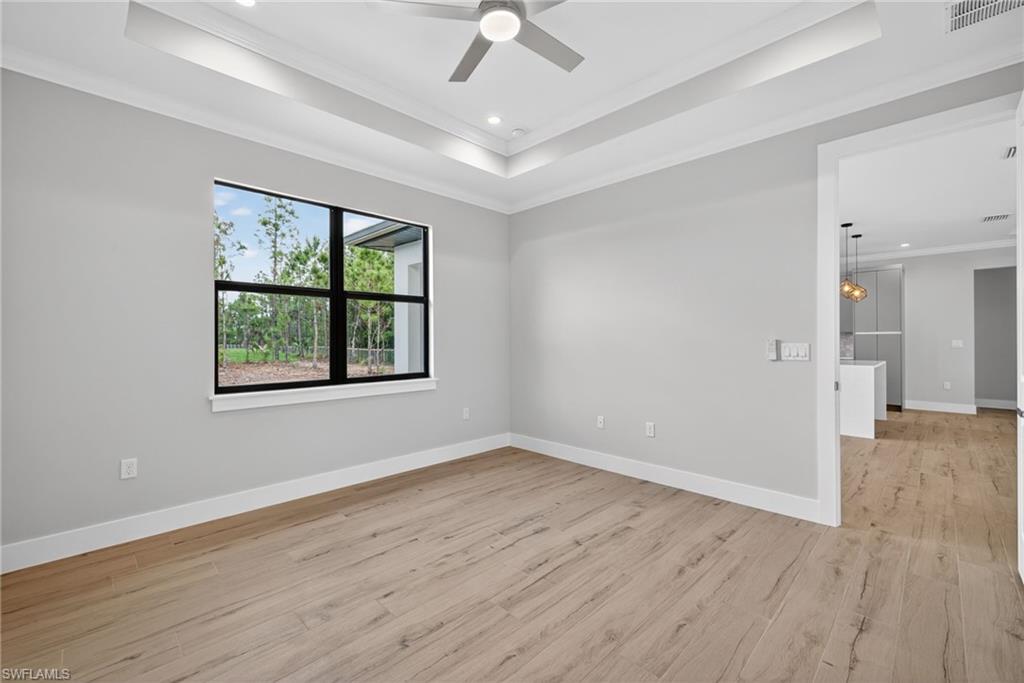 Spacious room featuring wood-finish flooring, a recessed tray ceiling with a modern ceiling fan, and a large window with black framing