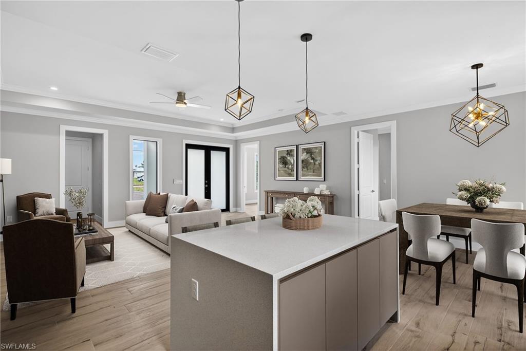 Open-concept kitchen and living area featuring a large center island with white quartz countertop, stainless steel appliances, wood-finish flooring, geometric pendant lighting, and abundant natural light from multiple glass doors and windows