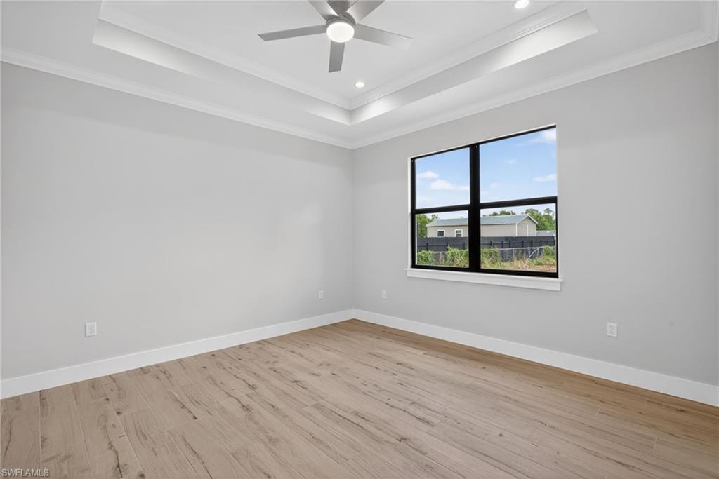 Spacious room featuring a tray ceiling with recessed lighting, wood-finish flooring, a contemporary ceiling fan, and a large window with black framing