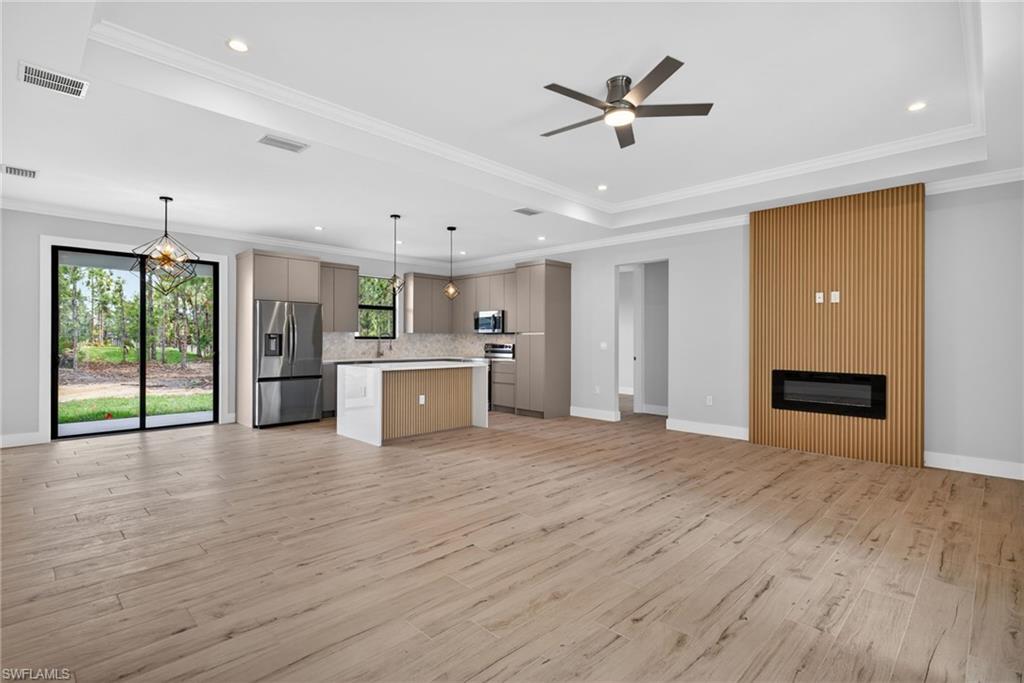 Open-concept living area featuring wood-finish flooring, a modern linear fireplace with a slatted wood-paneled accent wall, and a tray ceiling with recessed lighting