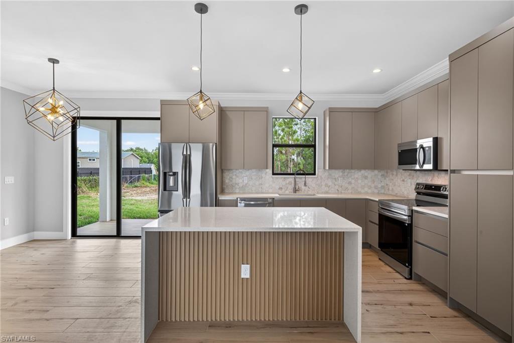 Open-concept kitchen featuring an island with a quartz countertop, recessed panel cabinetry, stainless steel appliances, wood-finish flooring, and a sliding glass door leading to the exterior