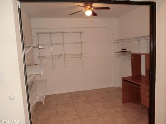 Room featuring tile flooring, white walls, built-in shelving, and a ceiling fan with light fixture