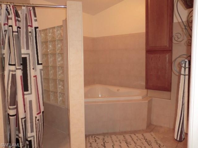 Corner soaking tub with tiled surround, adjacent to a shower enclosure with glass block wall, and upper wood-finish cabinetry