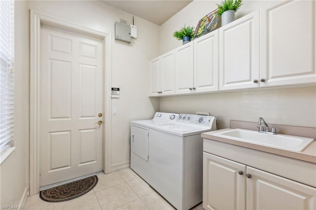 Laundry room featuring baseboards, light tile patterned floors, washer and dryer, cabinet space, and a sink