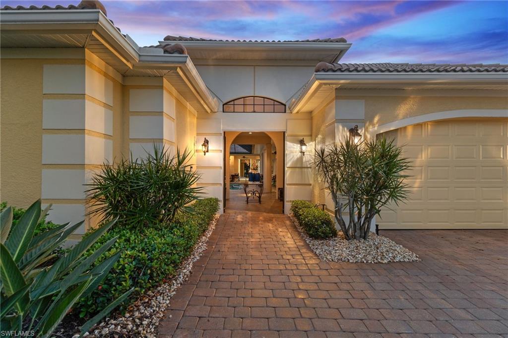 Exterior entry at dusk with a tiled roof, stucco siding, an attached garage, and decorative driveway