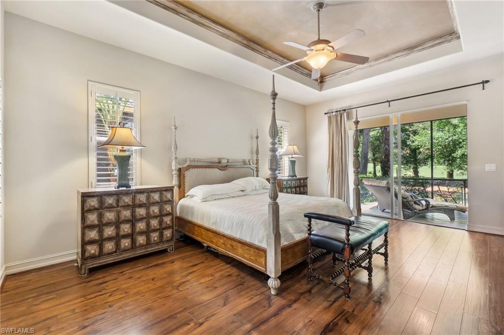 Bedroom featuring a ceiling fan, access to outside, hardwood / wood-style flooring, a tray ceiling, and baseboards