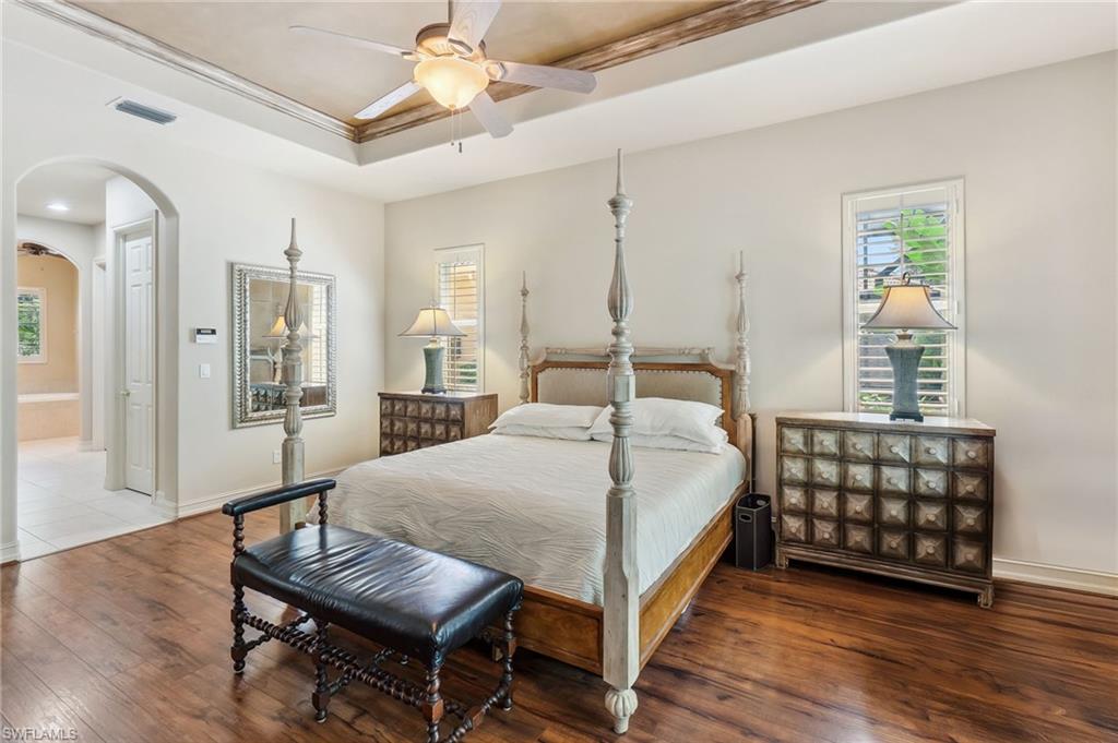 Bedroom with visible vents, baseboards, hardwood / wood-style floors, arched walkways, and a raised ceiling