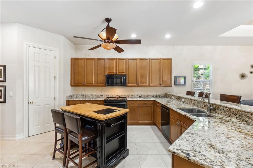 Kitchen with brown cabinets, black appliances, a sink, light stone countertops, and ceiling fan