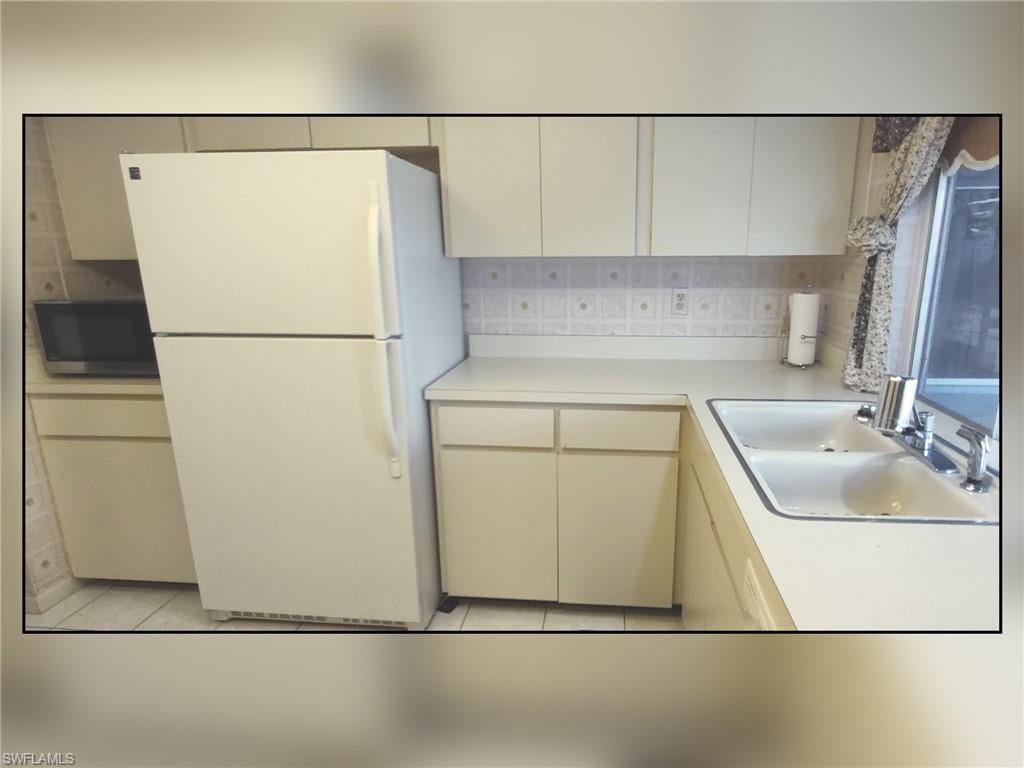 Kitchen featuring freestanding refrigerator, light countertops, stainless steel microwave, light tile patterned floors, and decorative backsplash