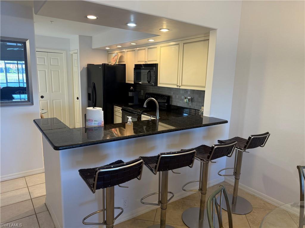 Kitchen with a breakfast bar area, black appliances, a peninsula, dark stone countertops, and light tile patterned flooring