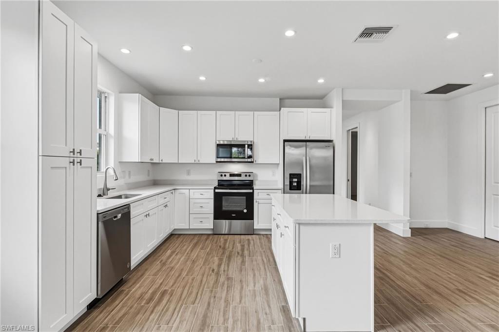 The kitchen showcases white shaker-style wood cabinetry, sparkling white quartz countertops, and a spacious island, all complemented by sleek stainless steel appliances. An additional window—thoughtfully added in this unique villa—floods the space with natural light, making this truly a one-of-a-kind offering.