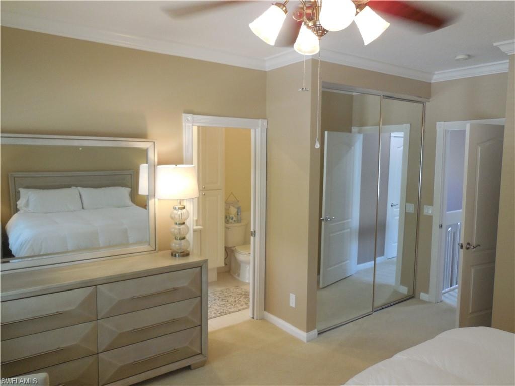 Bedroom with crown molding, light colored carpet, ensuite bath, baseboards, and a closet